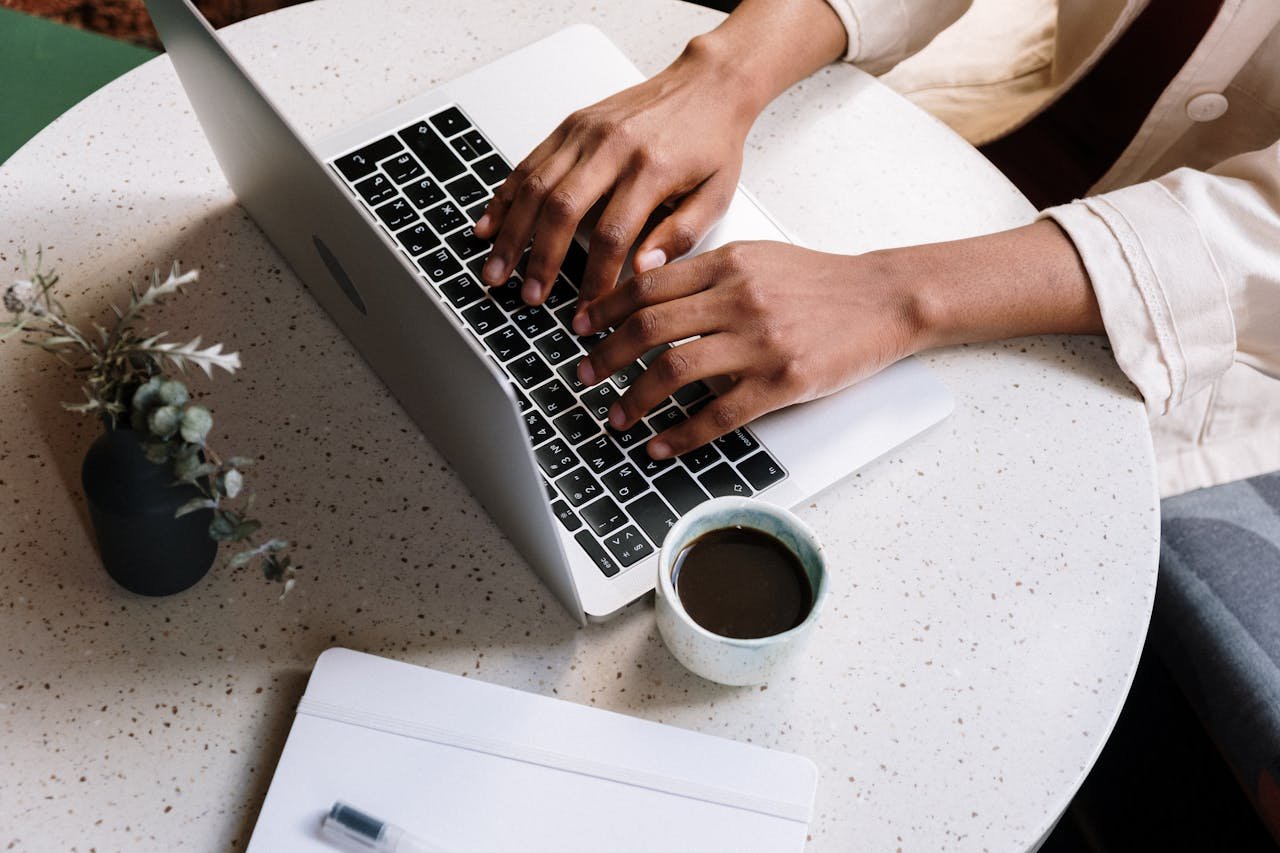 Crafting Captivating Headlines: Your awesome post title goes here A person typing on a laptop at a café table with coffee and a notebook.
